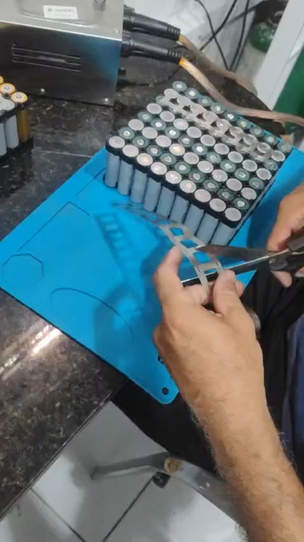 Fita de níquel sendo cortada para montagem de pack de bateria sobre tapete de bancada